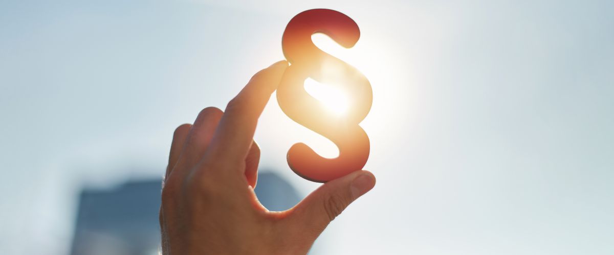 Paragraphen-Symbol wird gegen das Sonnenlicht gehalten – symbolisiert die gesetzlichen Änderungen für 2026 im Bereich Finanzen.