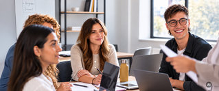Studierende arbeiten gemeinsam an einem Tisch mit Laptops und Notizen in einer Lern- oder Besprechungssituation.