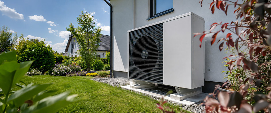 Außeneinheit einer Wärmepumpe an der Fassade eines Einfamilienhauses mit gepflegtem Garten – Symbolbild für die staatliche Förderung von Wärmepumpen und die Modernisierung energieeffizienter Heizsysteme.