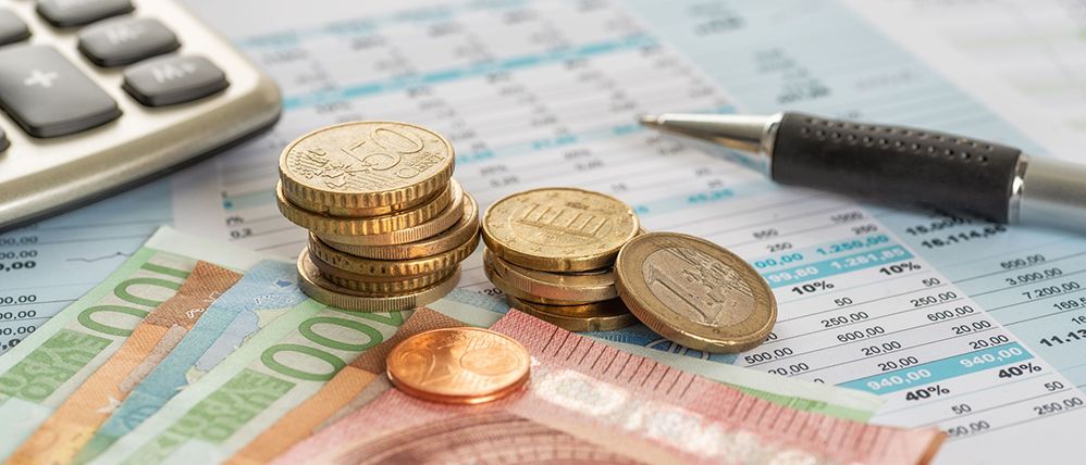 Münzen und Scheine auf Dokumenten und neben einem Kugelschreiber